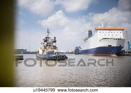 Stock Photo - Tugboat sailing in urban harbor. Fotosearch