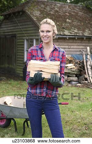 Stock Photo - Woman carrying firewood in backyard. Fotosearch
