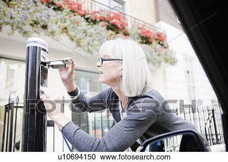 Stock Image - Woman charging electric car on street. Fotosearch