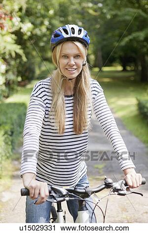 Stock Image - Woman riding bicycle on rural road. Fotosearch