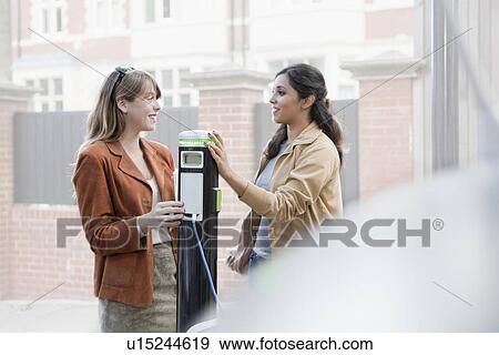 Stock Photo - Women charging electric car on street. Fotosearch