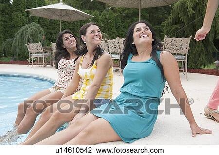 Stock Image - Women dangling feet in swimming pool. Fotosearch
