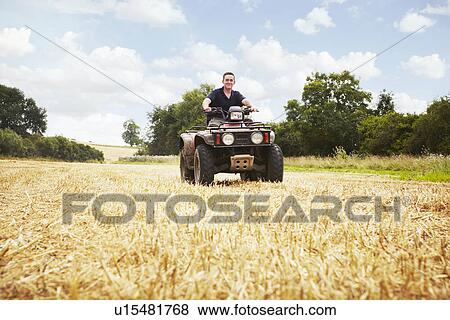 Stock Photo - Worker driving four wheeler in field. Fotosearch