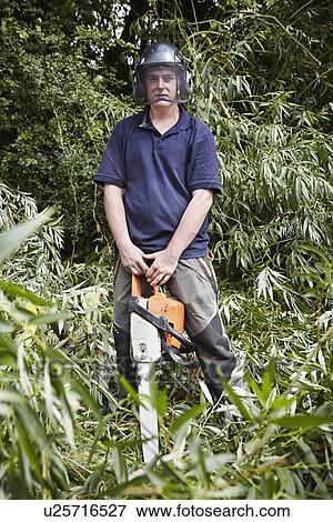 Stock Photo - Worker holding chainsaw in forest. Fotosearch