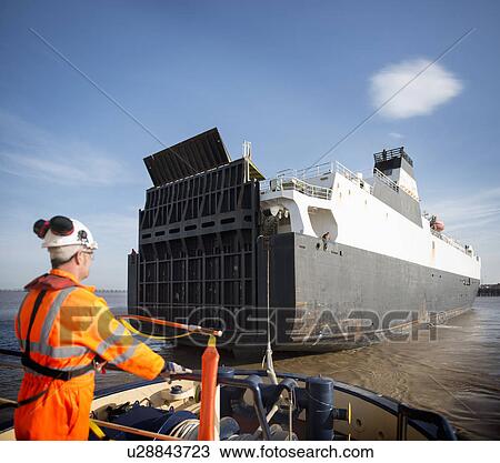 Stock Image - Worker on tug boat overlooking ship. Fotosearch