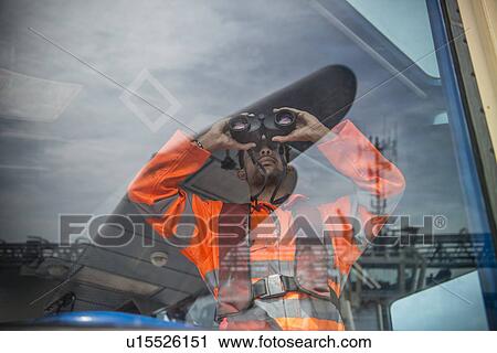 Stock Image - Worker on tug boat using binoculars. Fotosearch
