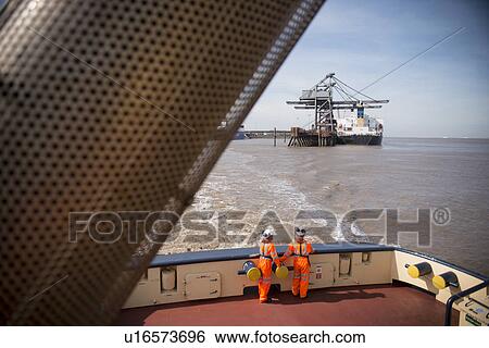 Stock Photograph - Workers on tug boat overlooking crane. Fotosearch