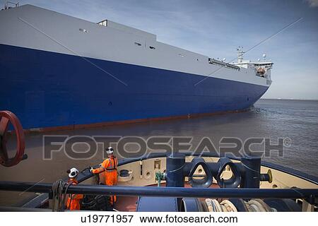 Stock Photo - Workers on tug boat overlooking ship. Fotosearch