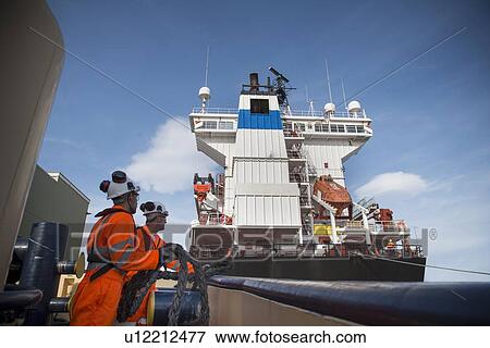 Stock Photo - Workers on tug boat pulling in rope. Fotosearch