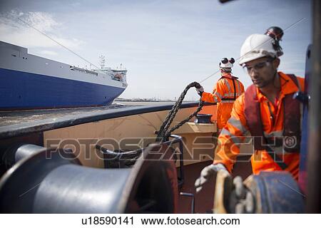 Stock Image - Workers on tug boat reeling in rope. Fotosearch