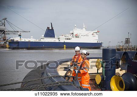 Stock Photography - Workers on tug boat tying rope. Fotosearch