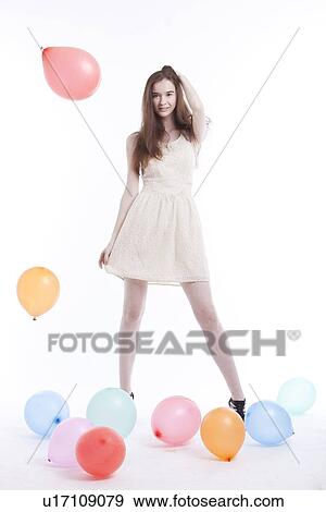 Stock Photo - Beautiful young woman in dress with balloons on floor against white background. Fotosearch