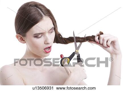 Stock Image - Beautiful young woman with scissors cutting her hair over white background. Fotosearch