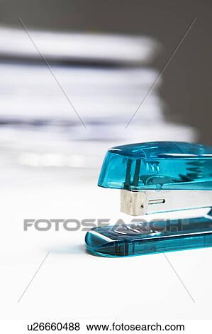 Stock Photo - Blue stapler on table with stack of papers in background. Fotosearch
