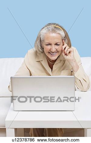 Stock Photograph - Cheerful senior woman using laptop for video calling. Fotosearch