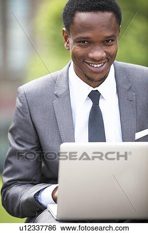 Stock Photograph - Close-up portrait of African American Businessman working on a laptop outdoors. Fotosearch
