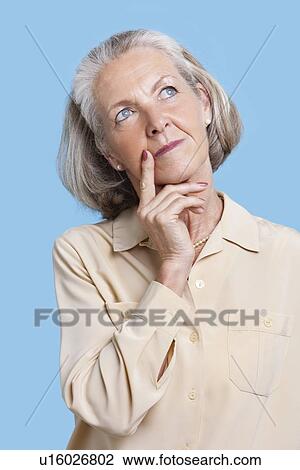 Contemplative senior woman in casuals with hand on chin against blue background View Large Photo Image Stock Image - Contemplative senior woman in casuals with hand on chin against blue background. Fotosearch