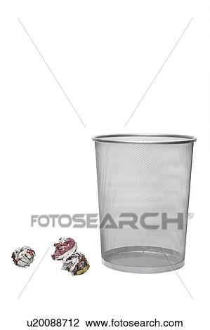 Stock Image - Crumpled papers next to empty wastebasket over white background. Fotosearch
