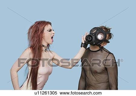 Stock Photography - Funky young woman slapping man in gas mask over blue background. Fotosearch