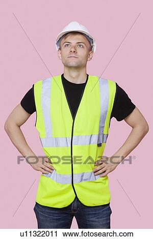 Handsome construction worker with hands on hips over pink background View Large Photo Image Stock Image - Handsome construction worker with hands on hips over pink background. Fotosearch