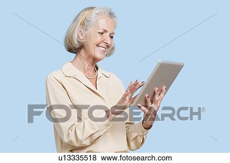 Happy senior woman using tablet PC against blue background View Large Photo Image Stock Photo - Happy senior woman using tablet PC against blue background. Fotosearch