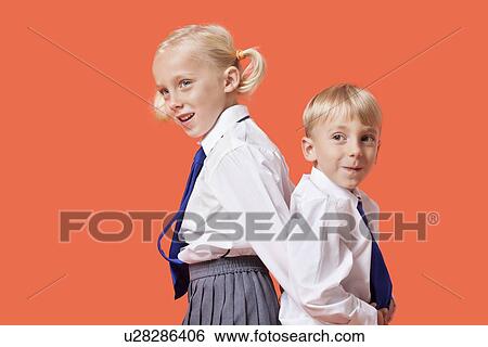 Happy young boy and girl in school uniform standing back to back over orange background View Large Photo Image Stock Photograph - Happy young boy and girl in school uniform standing back to back over orange background. Fotosearch