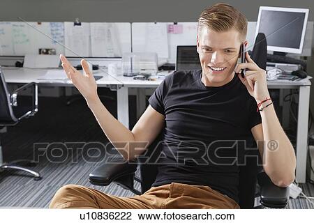 Stock Image - Happy young man using cell phone at office. Fotosearch