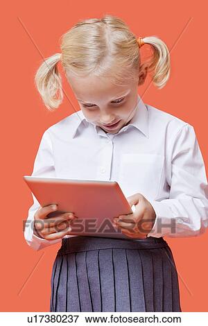 Happy young schoolgirl using tablet PC over orange background View Large Photo Image Stock Photo - Happy young schoolgirl using tablet PC over orange background. Fotosearch