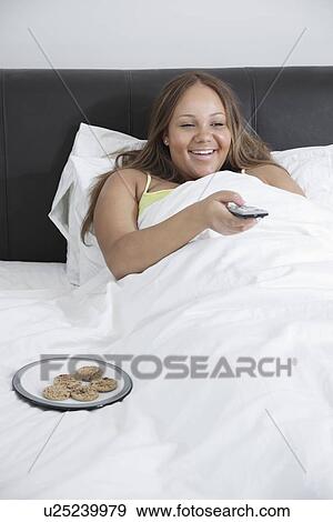 Happy young woman pregnant woman watching TV while lying in bed at home View Large Photo Image Stock Photo - Happy young woman pregnant woman watching TV while lying in bed at home. Fotosearch