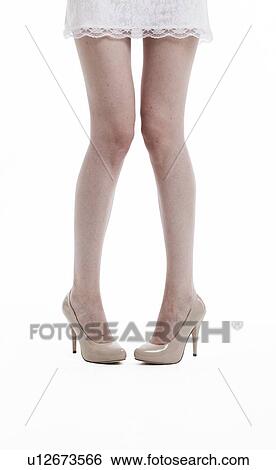 Stock Photograph - Low section of young woman in dress wearing high heels over white background. Fotosearch