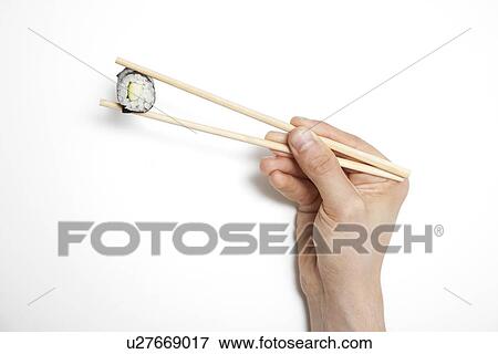 Stock Photo - Man's hand holding sushi roll in chopsticks against white background. Fotosearch