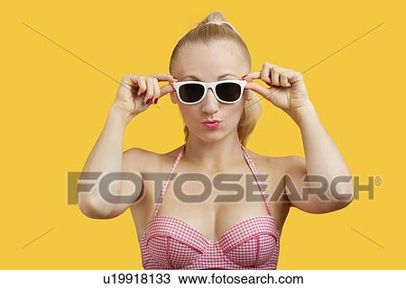 Portrait of a beautiful young woman in sunglasses puckering lips over yellow background View Large Photo Image Stock Image - Portrait of a beautiful young woman in sunglasses puckering lips over yellow background. Fotosearch