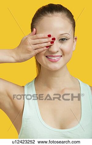Portrait of a beautiful young woman covering eye over yellow background View Large Photo Image Stock Image - Portrait of a beautiful young woman covering eye over yellow background. Fotosearch