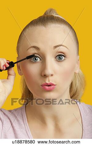 Portrait of a beautiful young woman applying mascara over yellow background View Large Photo Image Stock Image - Portrait of a beautiful young woman applying mascara over yellow background. Fotosearch