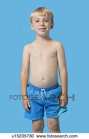 Stock Image - Portrait of a happy young boy in swim trunks over blue background. Fotosearch