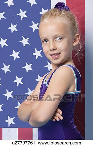 Stock Image - Portrait of a happy young female gymnast with arms crossed standing in front of American flag. Fotosearch