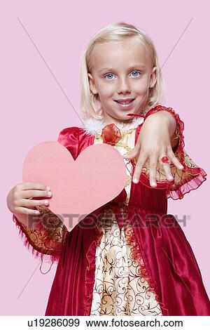 Portrait of a happy young girl dressed in princess costume holding paper heart as she displays ring over pink background View Large Photo Image Stock Photo - Portrait of a happy young girl dressed in princess costume holding paper heart as she displays ring over pink background. Fotosearch
