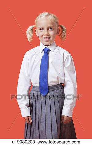 Stock Image - Portrait of a happy young girl in school uniform over orange background. Fotosearch
