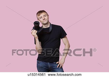 Portrait of a happy young male photographer holding camera over pink background View Large Photo Image Stock Image - Portrait of a happy young male photographer holding camera over pink background. Fotosearch