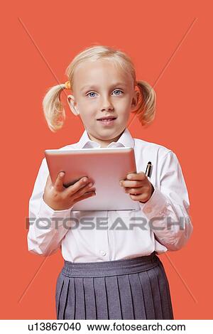 Portrait of a happy young schoolgirl holding tablet PC over orange background View Large Photo Image Stock Image - Portrait of a happy young schoolgirl holding tablet PC over orange background. Fotosearch