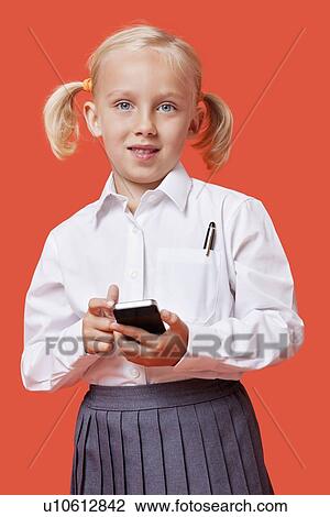 Stock Image - Portrait of a young schoolgirl holding cell phone over blue background. Fotosearch