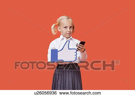 Portrait of a young schoolgirl with cell phone holding fake like button over orange background View Large Photo Image Stock Photograph - Portrait of a young schoolgirl with cell phone holding fake like button over orange background. Fotosearch