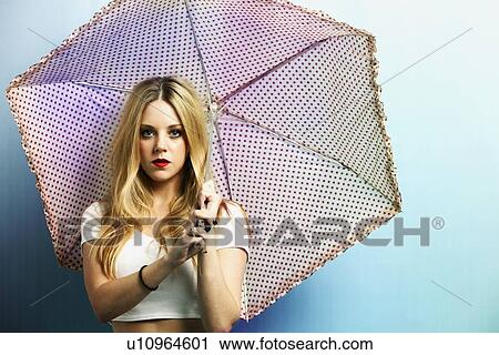 Stock Image - Portrait of a young woman with umbrella against blue background. Fotosearch