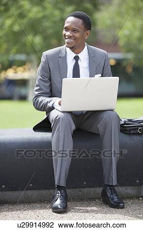 Portrait of African American Businessman working on a laptop outdoors View Large Photo Image Stock Image - Portrait of African American Businessman working on a laptop outdoors. Fotosearch