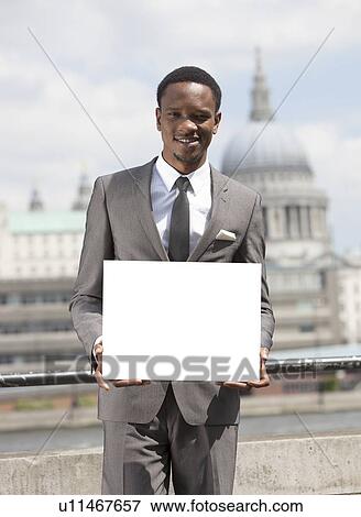 Stock Photo - Portrait of African American businessman smiling and holding blank cardboard. Fotosearch