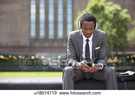 Stock Photo - Portrait of African American Businessman listening to music with headphones outdoors. Fotosearch