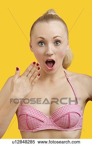Stock Photography - Portrait of amazed young woman with mouth open against yellow background. Fotosearch