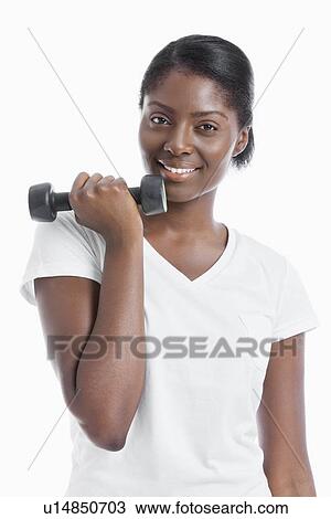 Stock Image - Portrait of an African American young woman with dumbbell over white background. Fotosearch
