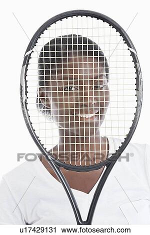 Stock Image - Portrait of an African American young woman looking through tennis racket. Fotosearch