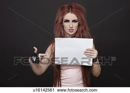 Stock Image - Portrait of arrogant young funky woman pointing towards blank placard against black background. Fotosearch